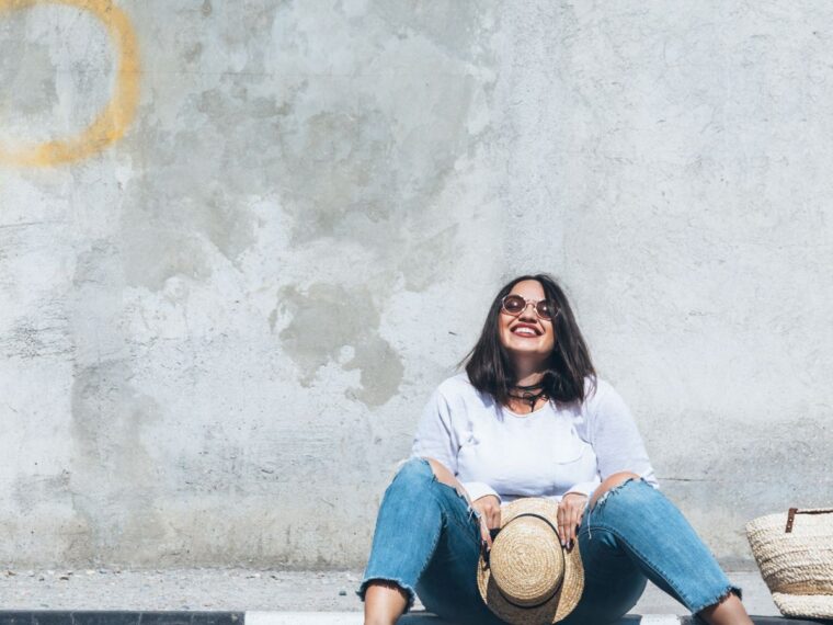 Girl in a white tee shirt and jeans and yellow heels sitting on a curb smiling