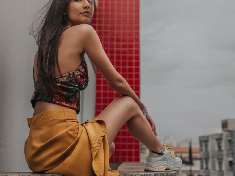 A girl sitting on a wall wearing a skirt and sneakers