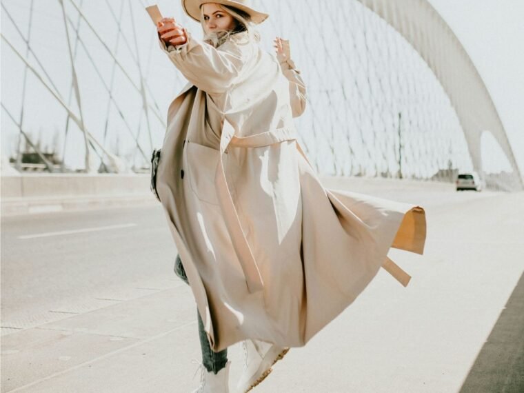 A girl standing with her trench coat blowing in the wind